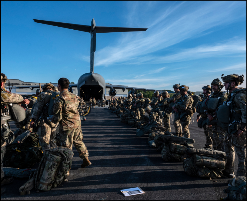 Soldiers in uniform in the foreground with a grounded military aircraft in the background.